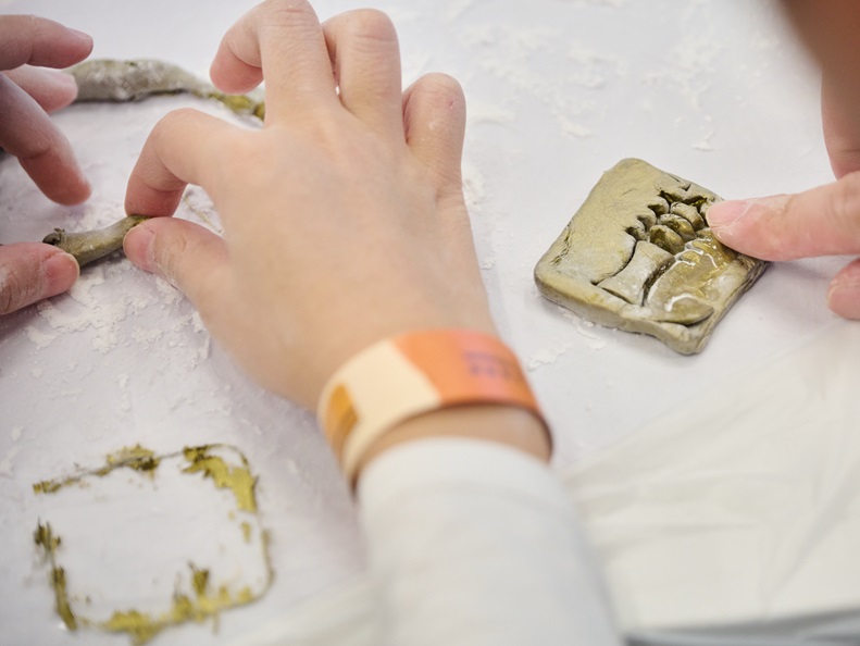 Children participants collaborating with their parents in shaping unique clay amulet for their necklaces.